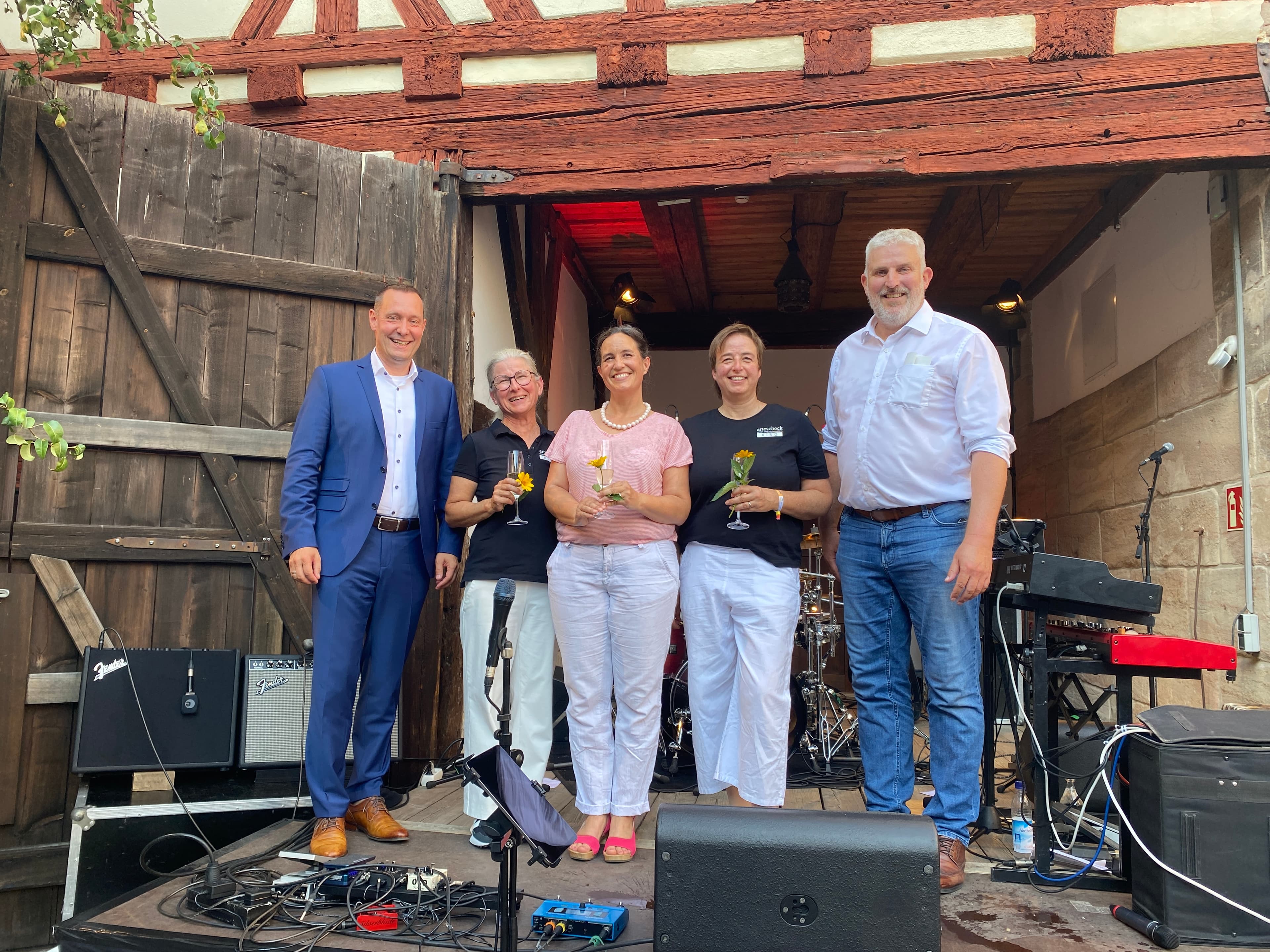 Andreas Kirchmayer/ Stadt Lauf Zwei Wochen Kulturhighlights im Spitalhof Open-Air-Kino, Lesungen, Konzerte: das alles und mehr ist auch dieses Jahr bei der Veranstaltungsreihe "Sommer in Lauf" im Spitalhof geboten. Bei der Eröffnungsfeier am gestrigen Donnerstagabend stellten die drei Organisatorinnen, Dr. Ina Gombert von der Stadtbücherei sowie Nicole Reit und Viola Gellings vom Kulturverein arteschock e.V., das Programm vor. Sie bedankten sich bei allen Mitwirkenden, von den Künstlern über die Helfer, die Stadtverwaltung, die VHS und das Stadtarchiv für die Bereitstellung von Räumen, den DAV, den Biergarten auf dem Kunigundenberg und viele weitere für die Unterstützung. Viola Gellings betonte, dass das Kulturfestival ohne die Hilfe von vielen Ehrenamtlichen nicht stattfinden könnte. Parallel zum Programm im Spitalhof kann man derzeit die Plakatausstellung "Wie fühlt sich Demokratie für dich an?" der Initiative "(L)aufeinander zugehen" in der Stadtbücherei besuchen, wie Dr. Gombert erwähnte. Bürgermeister Thomas Lang, der die Schirmherrschaft für die Eröffnung übernommen hatte, sprach das besondere Ambiente des Spitalhofs an und lobte das hochwertige und abwechslungsreiche Programm des Festivals, das von der Stadtbücherei und arteschock e.V. zusammengestellt worden war. Auch der Bürgermeister bedankte sich bei allen Mitwirkenden, Sponsoren und Medienpartnern. "Lassen Sie uns aus diesem Sommer in Lauf etwas ganz Besonderes machen", wandte sich Lang an die zahlreichen Gäste, die zur Eröffnung gekommen waren, darunter seine beiden Stellvertreter Erika Vogel und Daniel Illauer, viele weitere Stadtratsmitglieder, Beate Treffkorn von der Unternehmenskommunikation der Sparkasse Nürnberg, ihren Vorgänger Otfried Bürger, Lambert Herrmann vom Verlag Hans Fahner, einem der Medienpartner, Vertretern der Abteilung Kultur und Freizeit der Stadtverwaltung, der Laufer Kulturszene und der Laufer Wirtschaft. Landrat Armin Kroder, der mit dem Bürgermeister auf die Bühne gekommen war, freute sich, dass es bei der Eröffnung der sechsten Ausgabe von "Sommer in Lauf" erstmals nicht regnete. Den Spitalhof bezeichnete er als einen der schönsten Plätze in ganz Mittelfranken. Kroder gratulierte zum 30. Geburtstag des Kulturvereins arteschock e.V., der am 25. Juli in der Wenzelburg gefeiert wird, und wünschte der ganzen Veranstaltungsreihe viele Besucherinnen und Besucher. Wolfgang Fink begleitete die Eröffnung am Klavier. Im Anschluss sorgten UI•IO & Bourbon Street für das erste musikalische Highlight der Veranstaltungsreihe. "Das Konzert war sehr gut besucht, die Stimmung war super. Ein idealer Auftakt für unseren Open-Air-Kultursommer", sagt Dr. Ina Gombert. Das Programm von Sommer in Lauf finden Sie hier: https://www.sommer-in-lauf.de