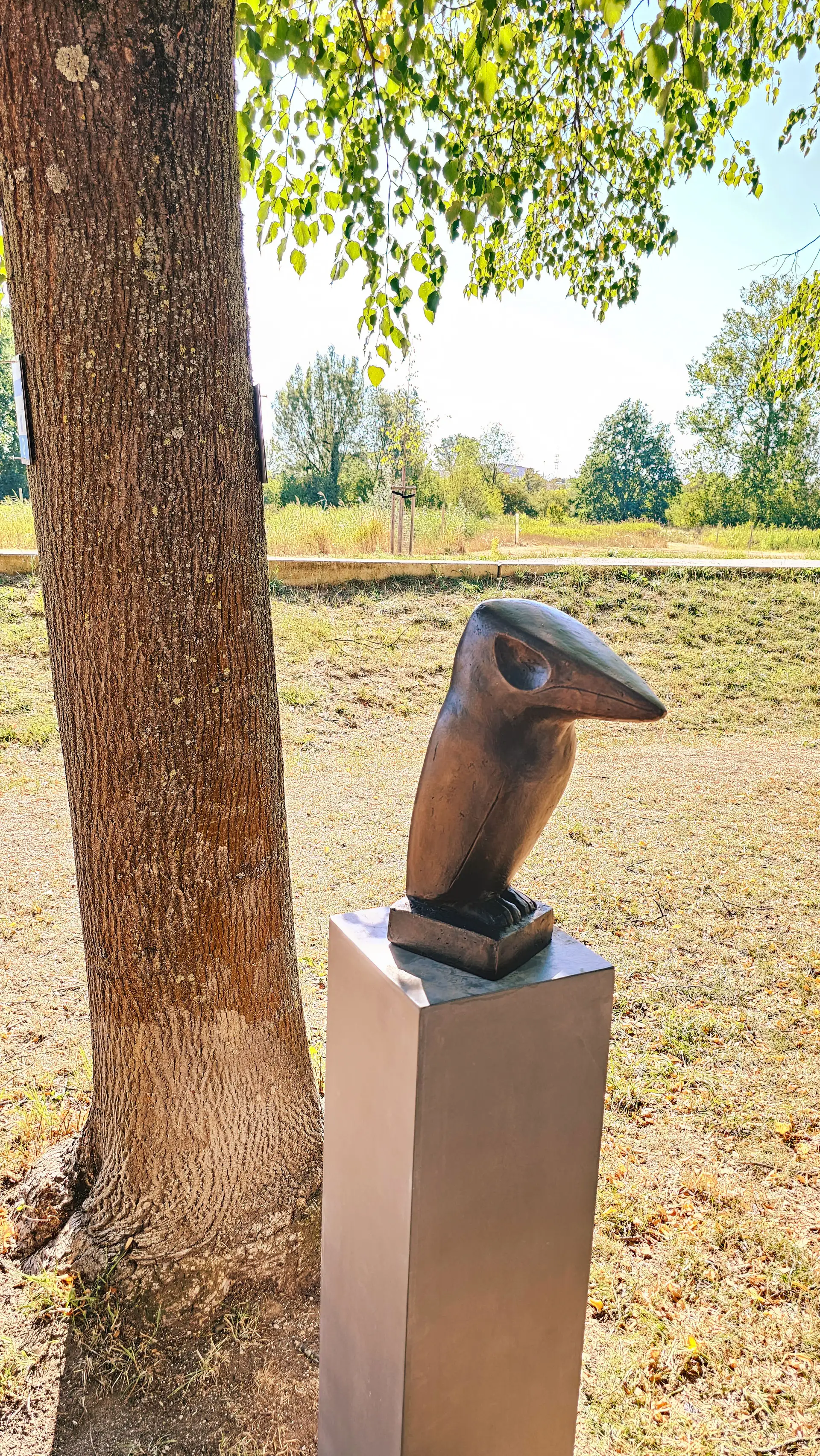 Bronzene Skulptur eines Eisvogels auf einem Sockel mit kleinen Wasserelementen oder Steinen.