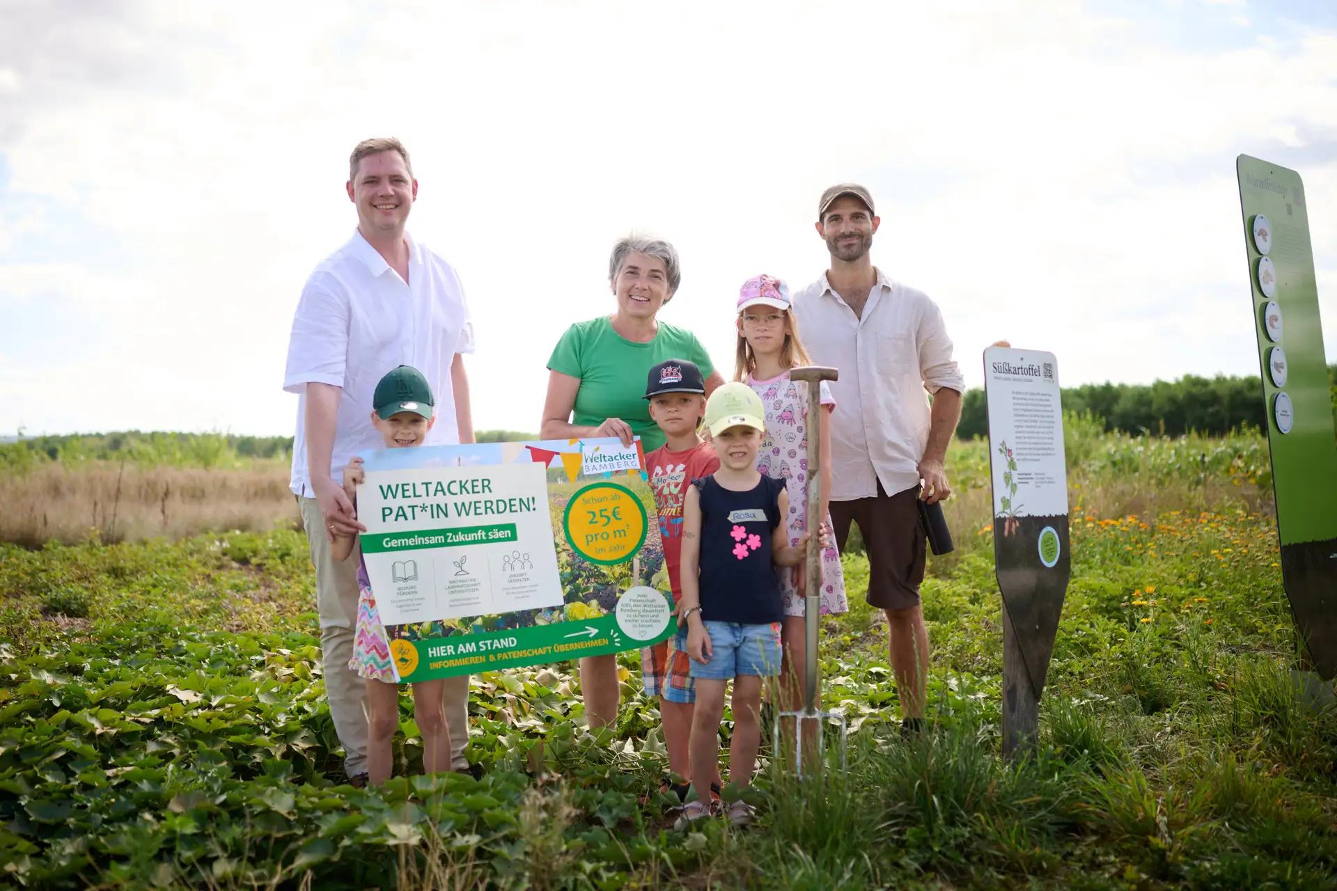 Person auf einem Feld vor einem Schild, im Hintergrund landwirtschaftliche Flächen und Vegetation.