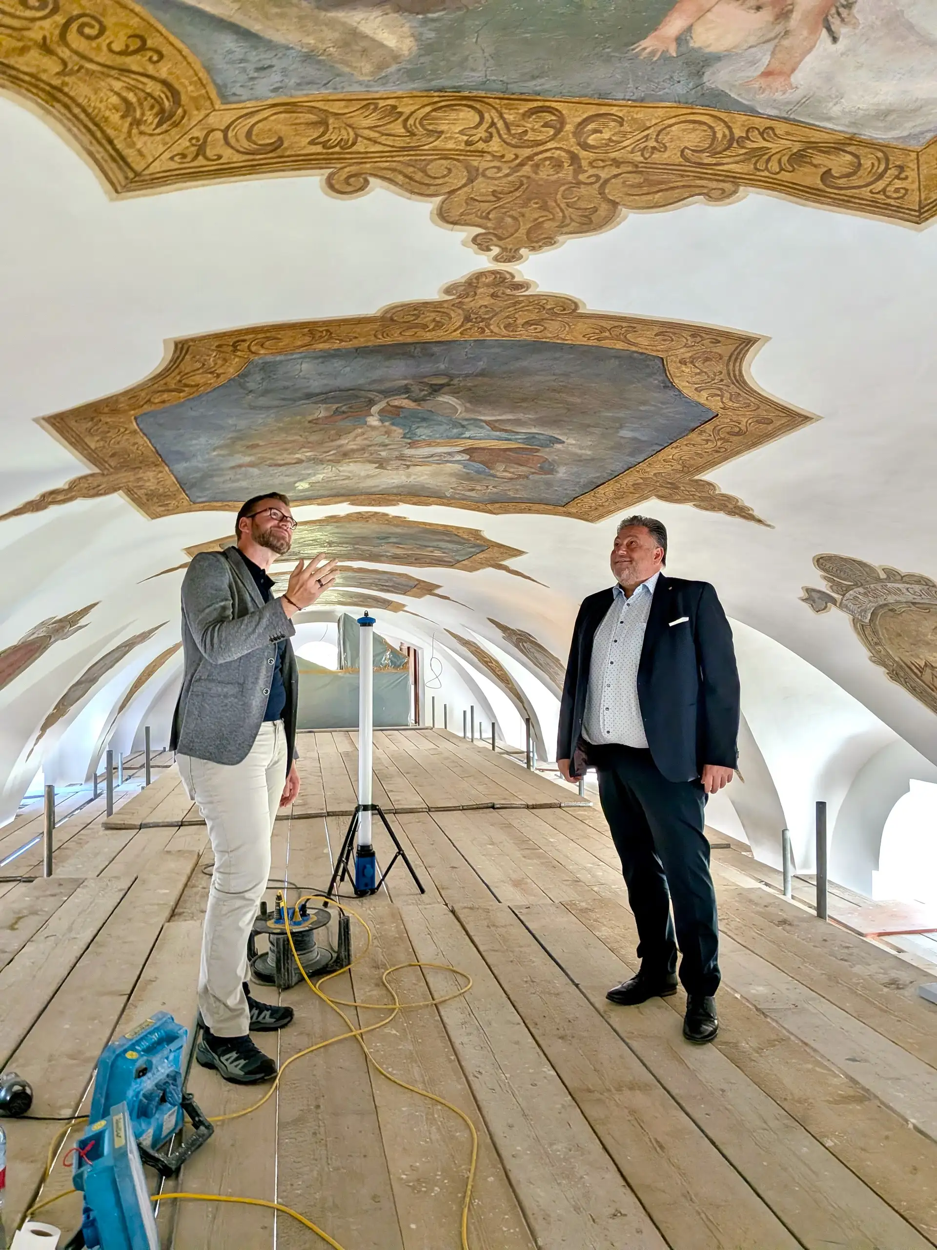 Personen besichtigen die restaurierten Deckengemälde in der Kirche Saltendorf; Blick auf einen Abschnitt der bemalten Decke.