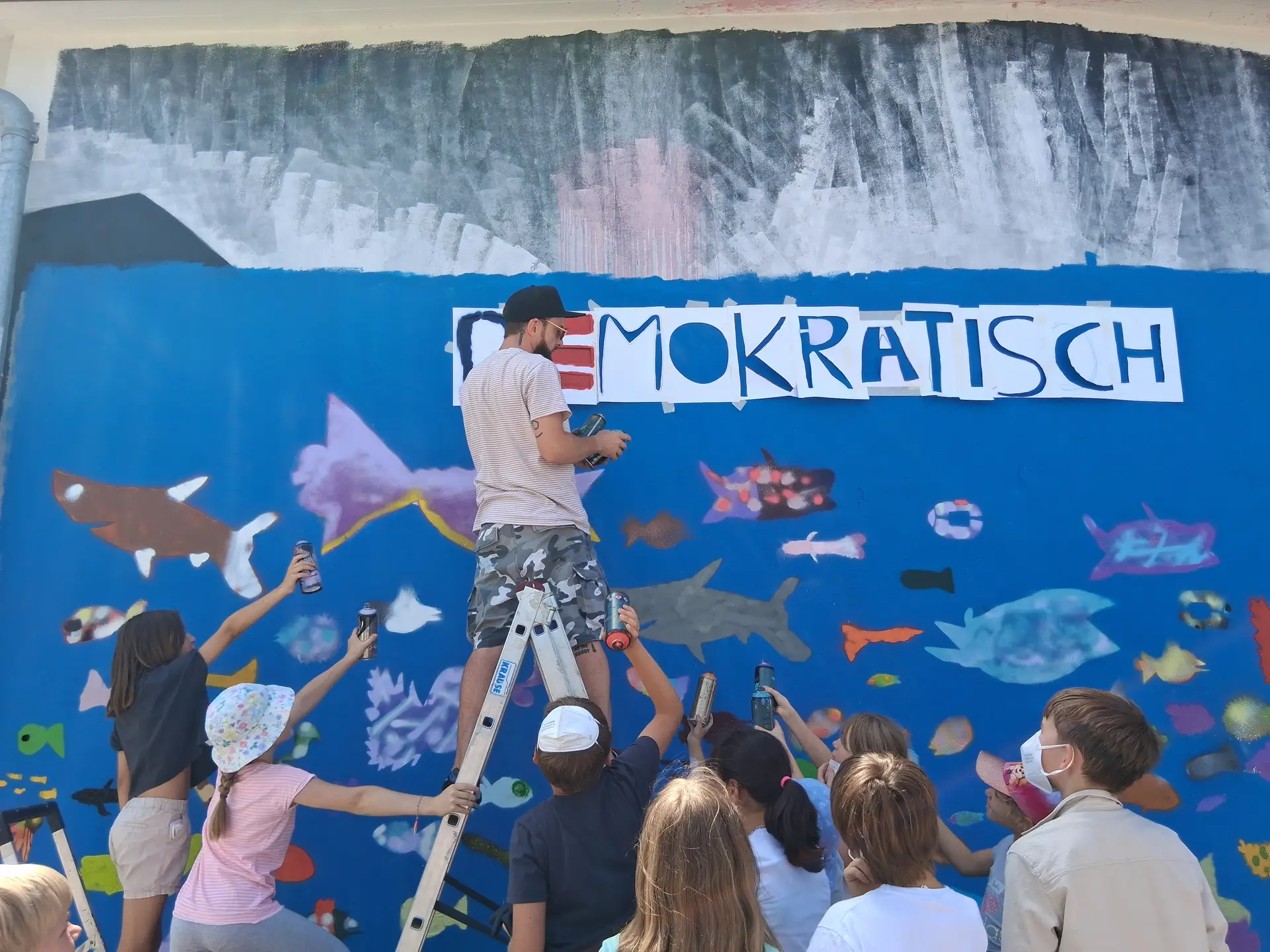 Farbenrausch in der Unterwasserwelt: Graffiti-Künstler Martin Keindl leitete die Kinder bei der Umsetzung ihrer kreativen Ideen an, die Kinder reichten ihm die Spraydosen für den Schriftzug.