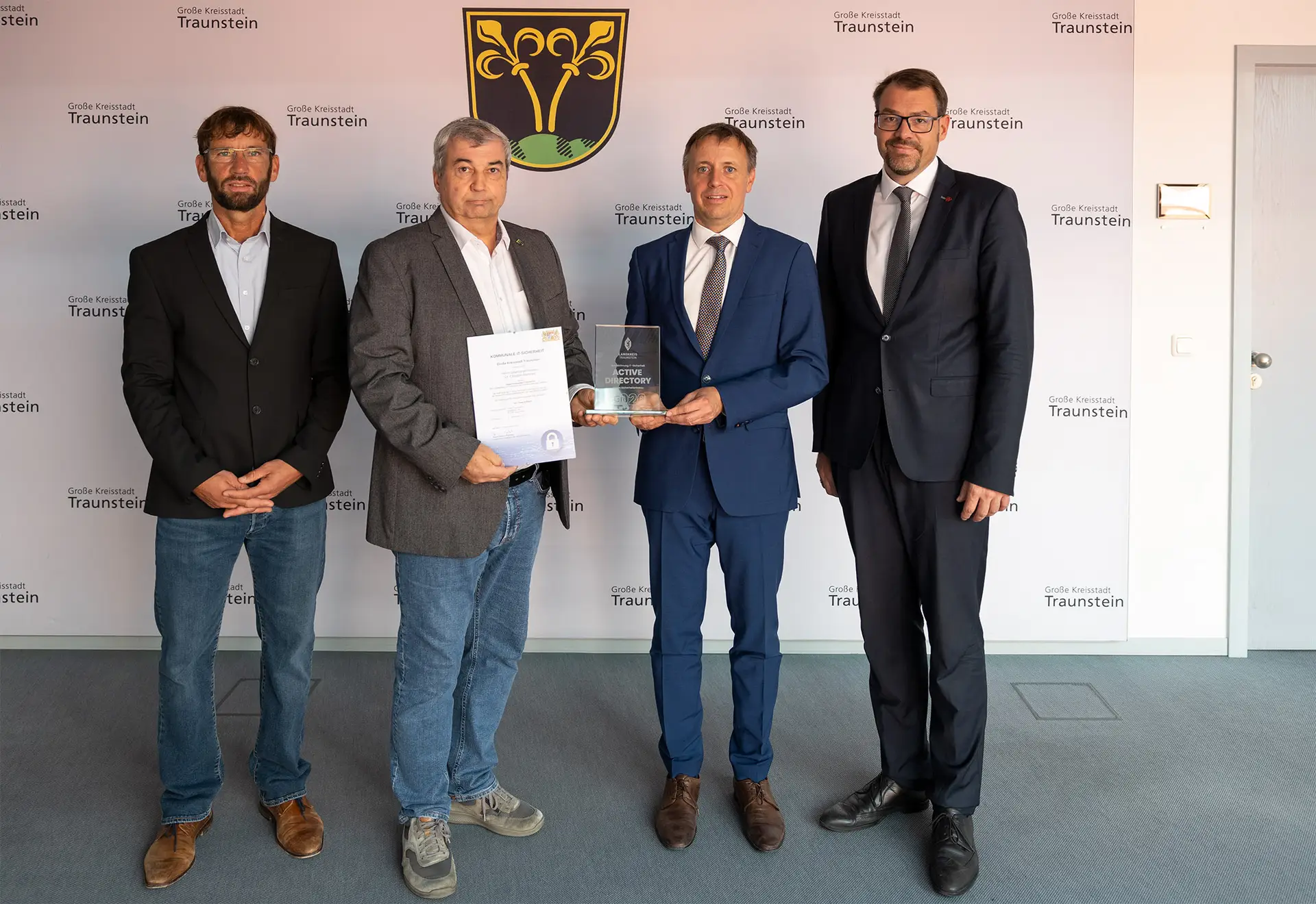 Eine Gruppe von vier Personen posiert nebeneinander, darunter ein Oberbürgermeister, während sie gemeinsam eine Auszeichnung bzw. ein Siegel zur Cybersicherheit präsentieren.